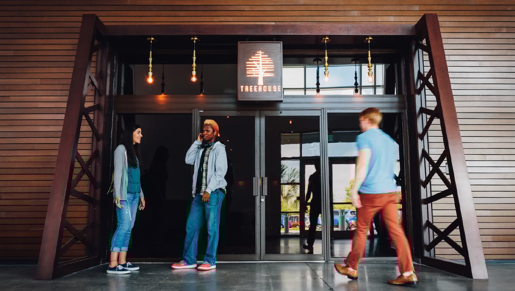 Students chat outside the Treehouse entrance, a cozy campus venue for events, performances, and gatherings.