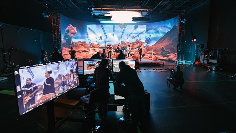 Students work on computers in front of an LED backdrop displaying a desert set in Studio V1: Virtual Production.