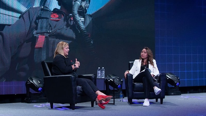 Sheena Fowler on stage with Dr. Haifa Maamar in the Full Sail University Orlando Health Fortress, an image of a fighter pilot in a cockpit is displayed on screen behind them.
